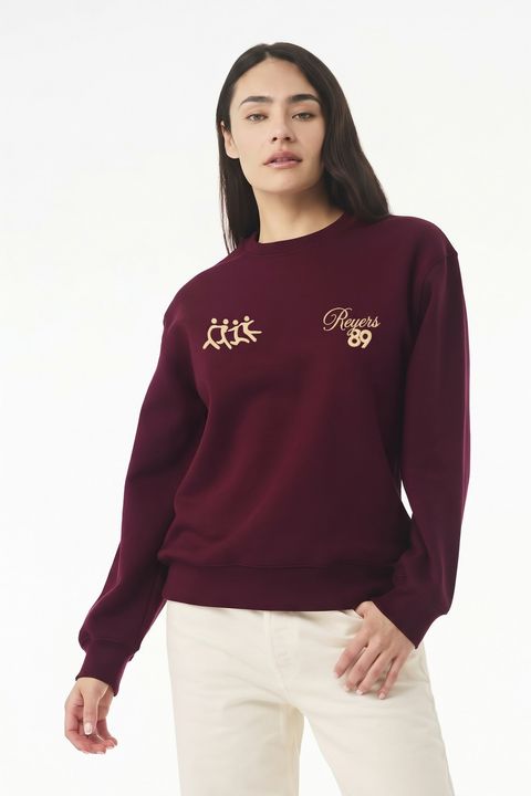 Une personne porte le pull Reyers89 bordeaux, vu de face, logos crème sur la poitrine